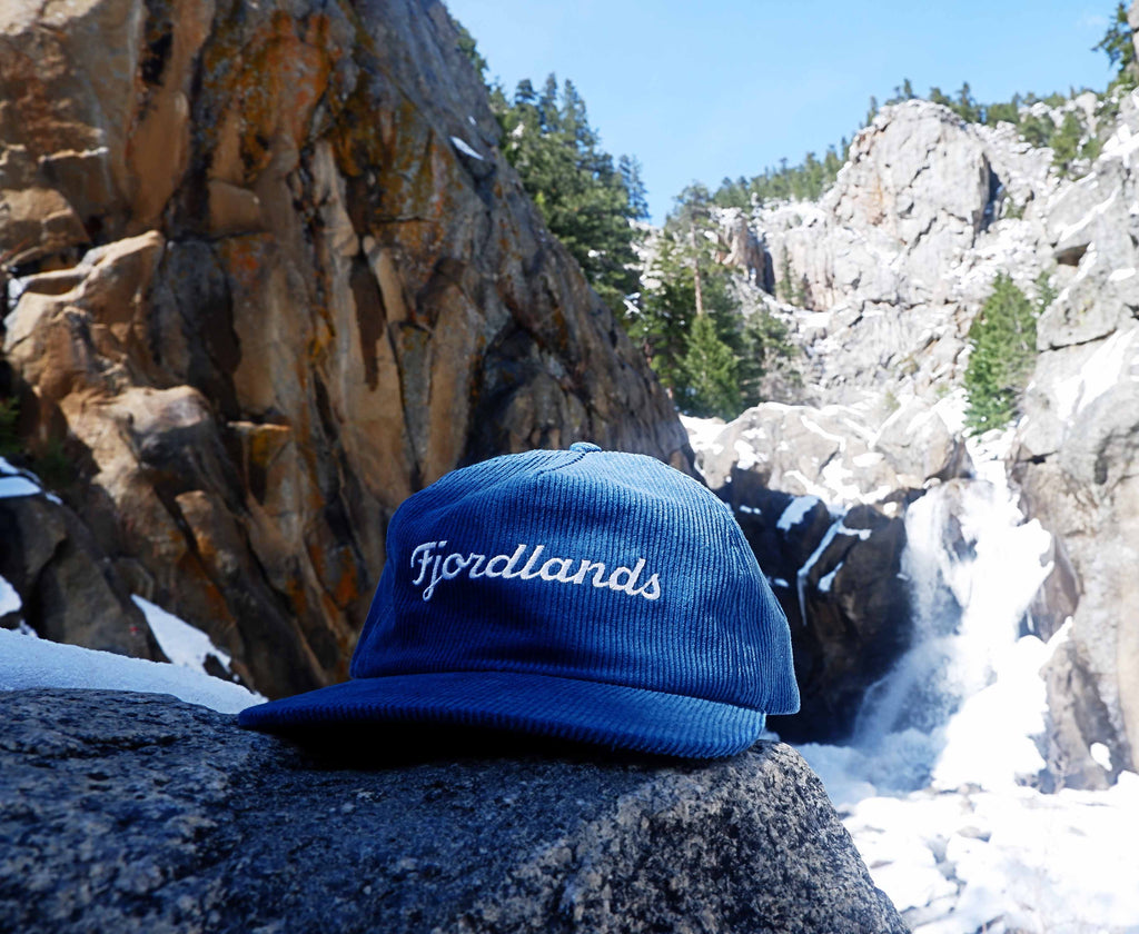 Fjordlands Cord Hat against waterfall backdrop.